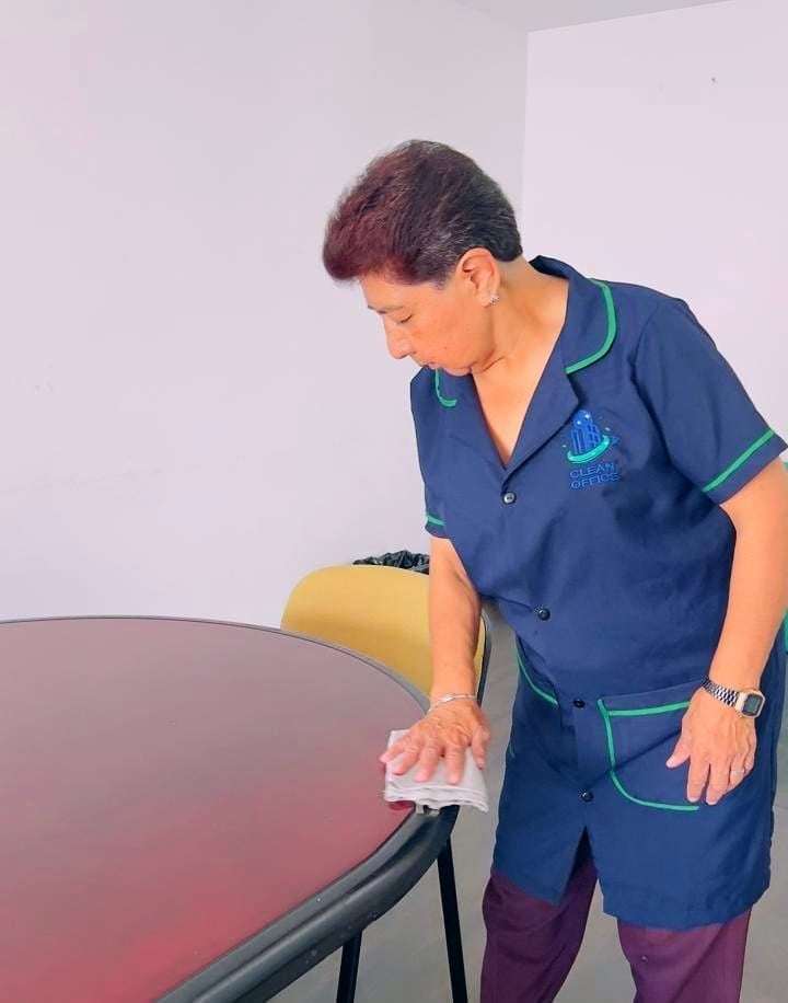 Healthcare worker in navy scrubs cleaning a red table surface with a cloth indoors